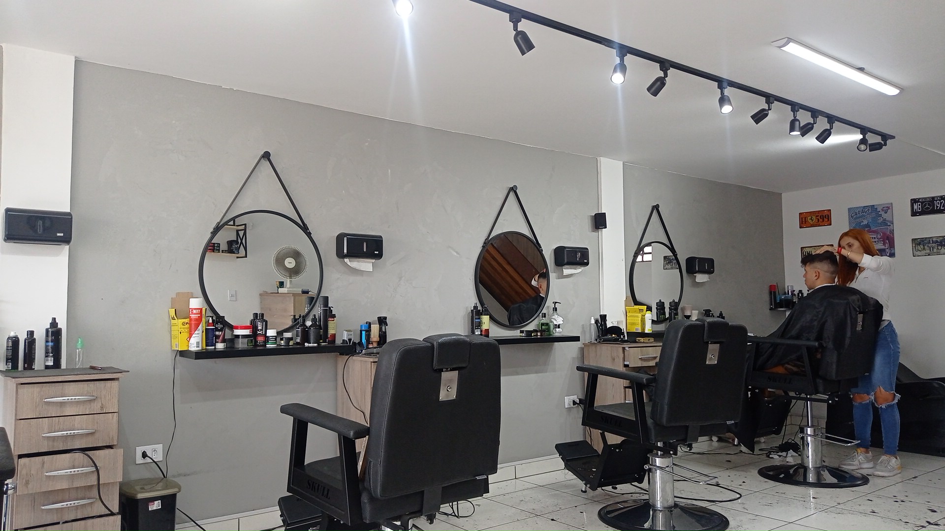 Interior da Barbearia Garage Pilarzinho, com as cadeiras, espelhos redondos e barbeiros atendendo